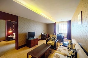 A living room with a sofa, a TV, a wooden coffee table, and a dining area with a table and chairs.