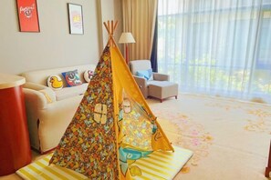 A living room with a sofa, a chair, a colorful teepee, and a lamp.