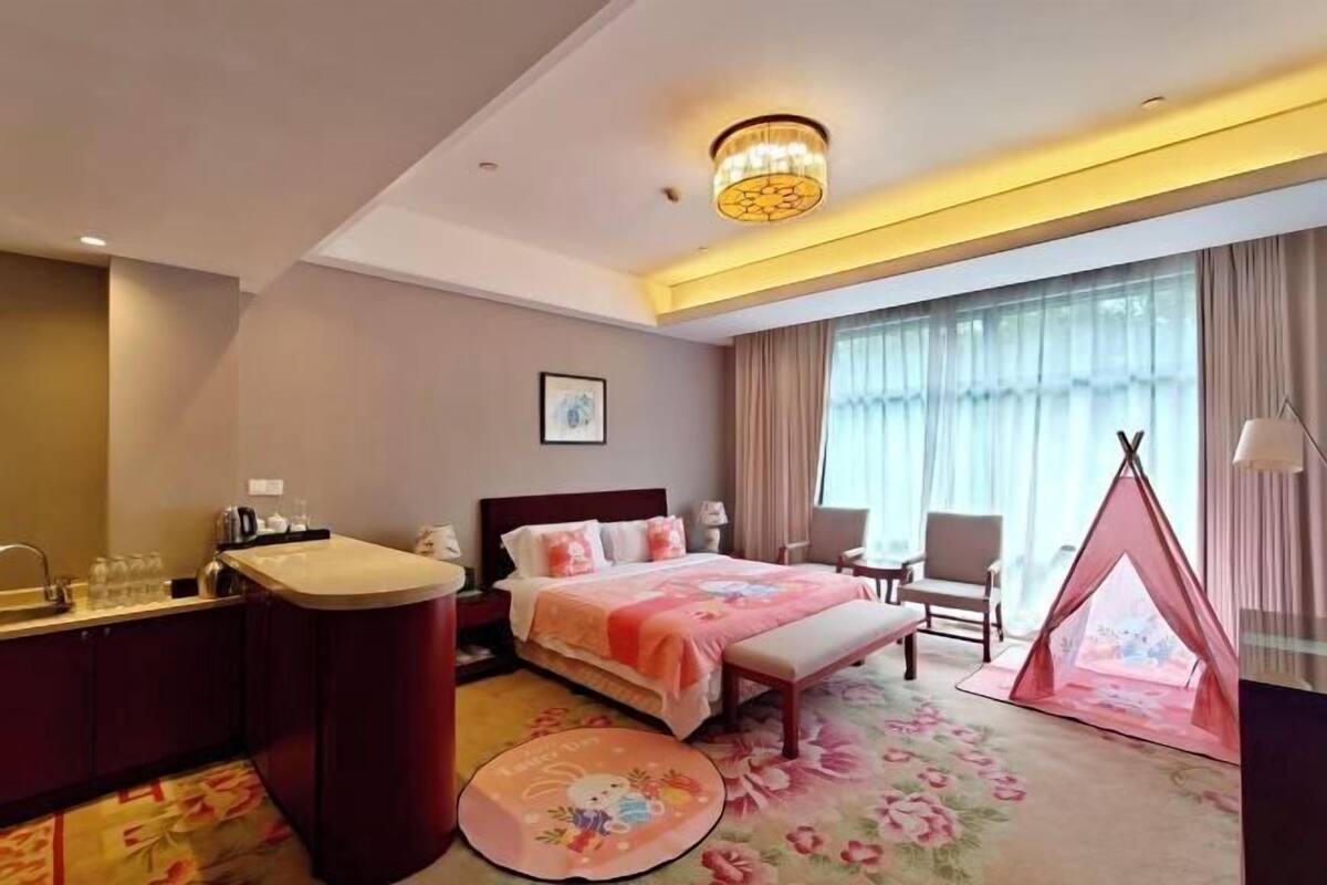A hotel room with a bed, bedside table, chair, window, and a tent-like structure.