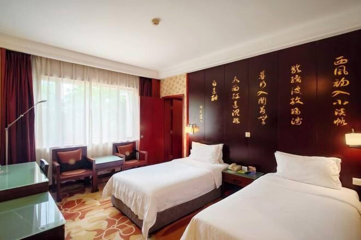 A hotel room with two beds, a desk, a chair, and a large window with curtains.