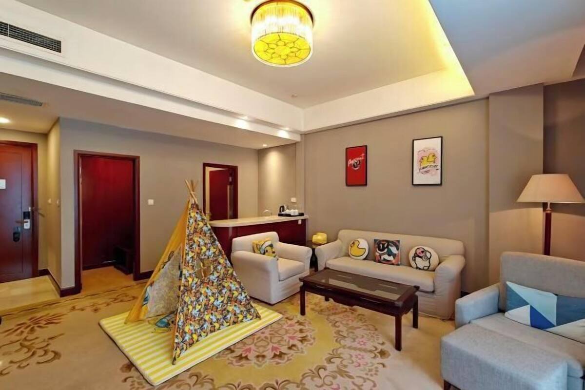 A hotel room with a living area, a sofa, a coffee table, a lamp, a fireplace, and a door.