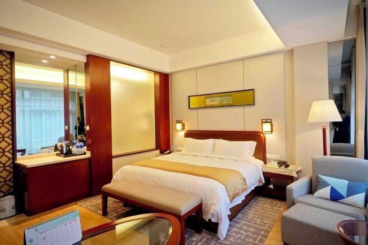 A hotel room with a bed, bedside table, chair, desk, and a mirror.