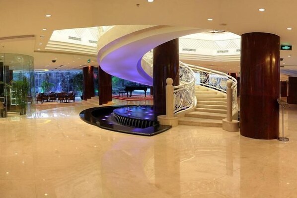 A spacious lobby with a grand staircase, a water feature, and a piano.
