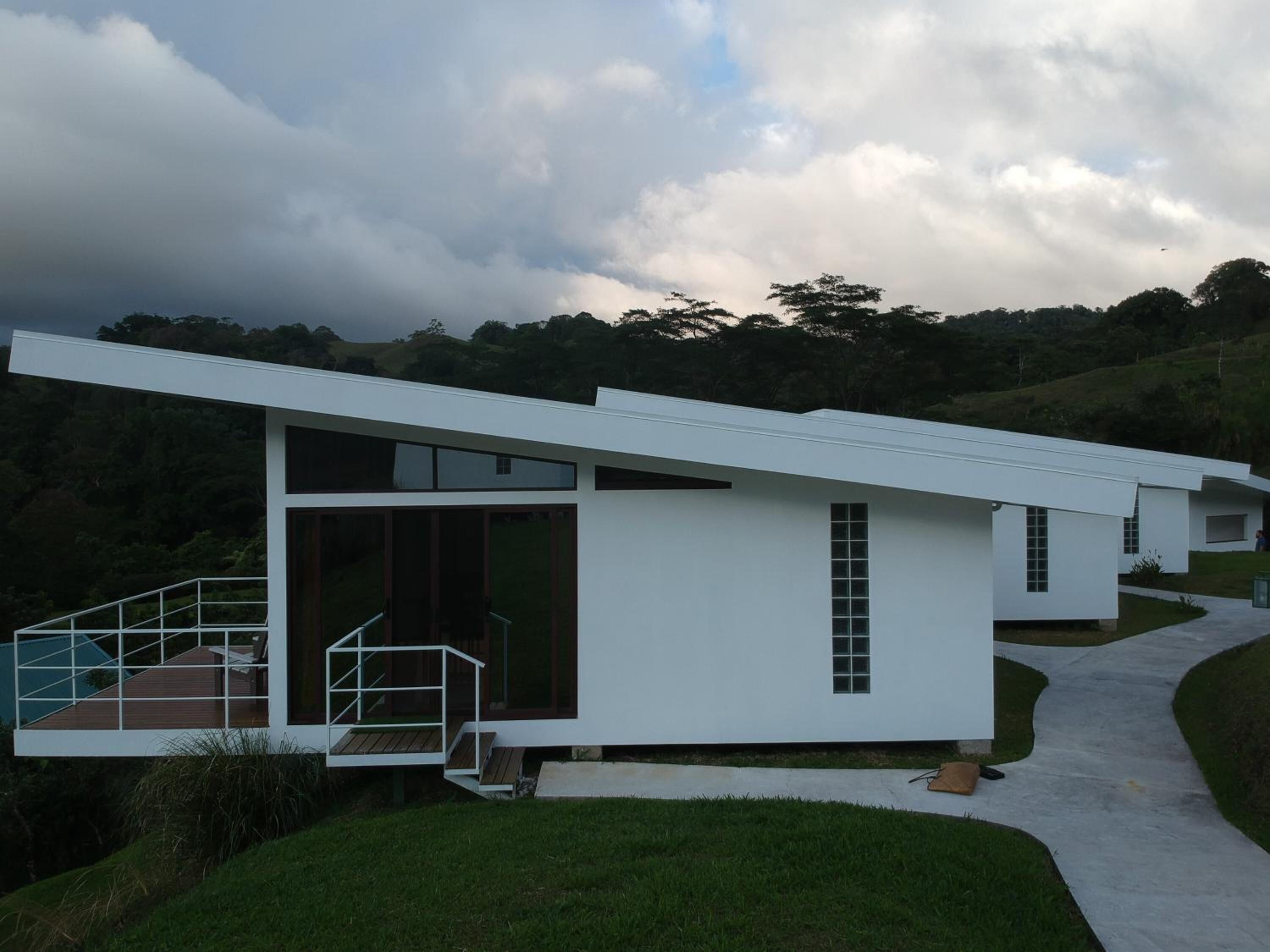 A modern, white, two-story house with a flat roof, large windows, and a visible staircase leading to a deck.