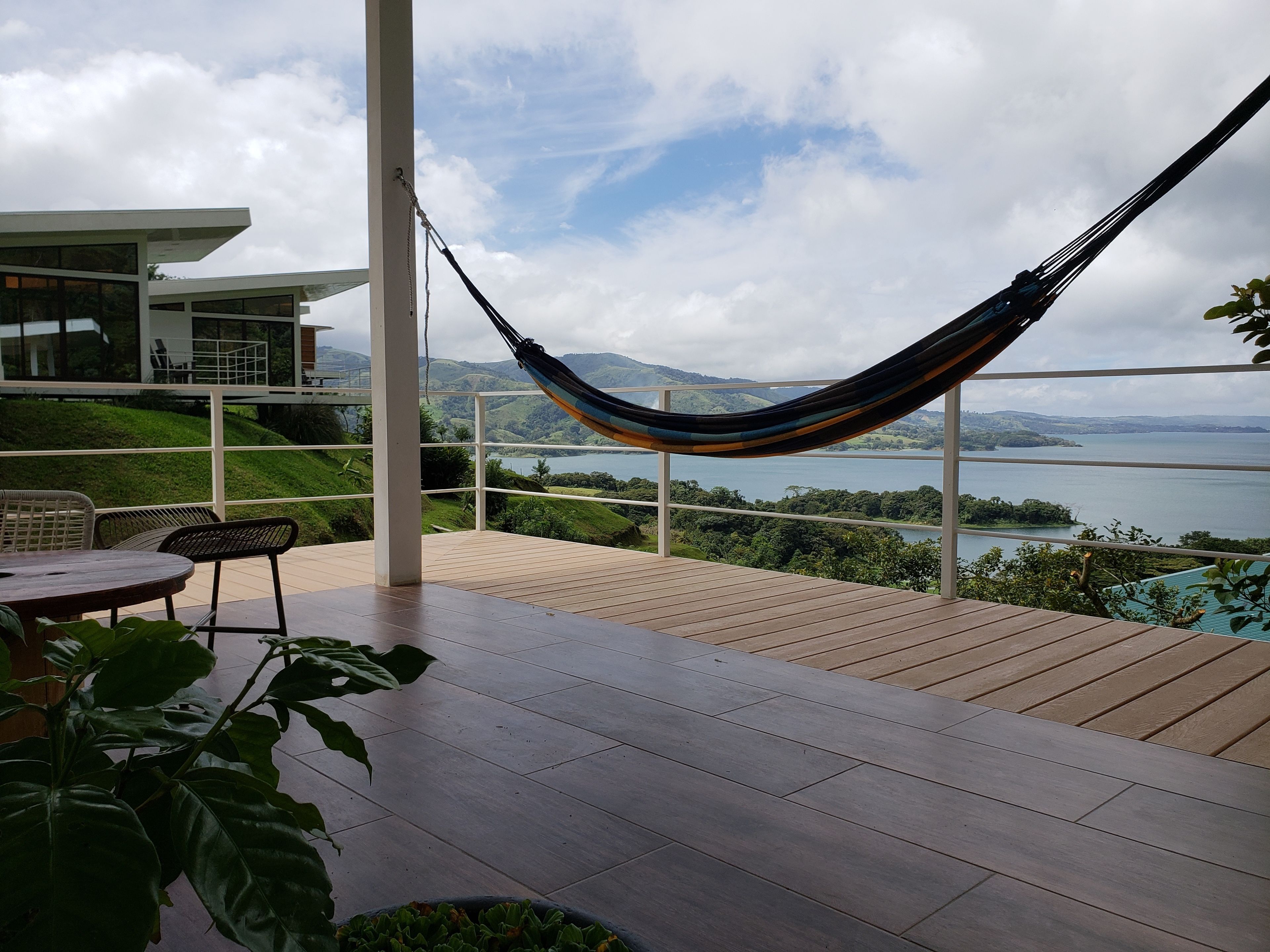 A hammock on a wooden deck overlooking a lake with mountains in the distance.