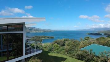 Une maison moderne dotée d’une grande baie vitrée donnant sur un lac pittoresque et des collines.