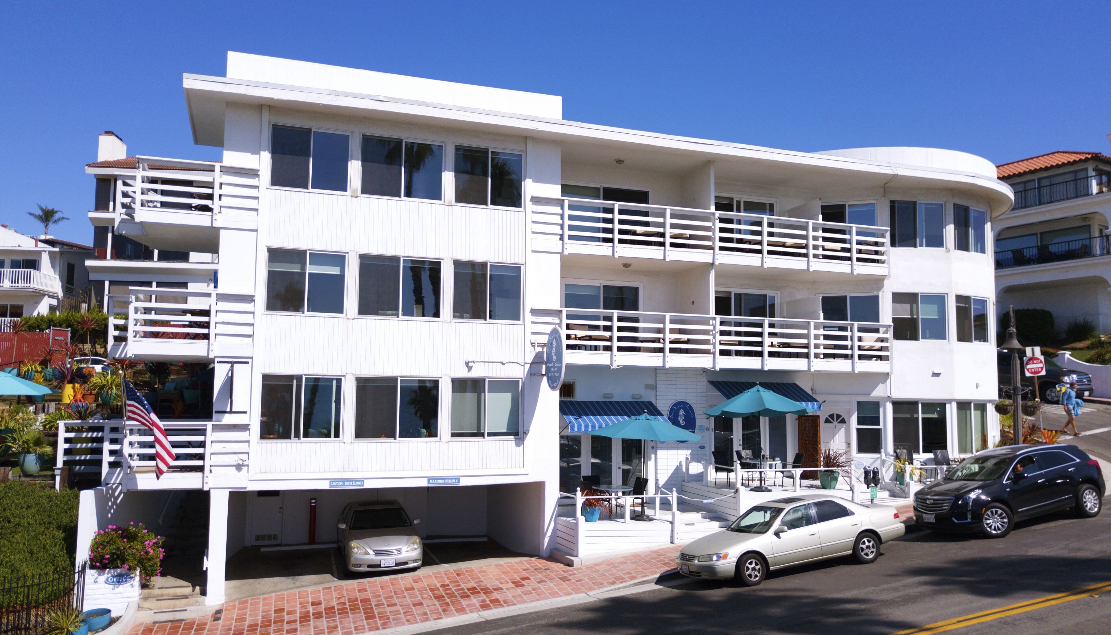 Un hôtel à plusieurs étages, doté d’une façade blanche, de balcons et d’un espace extérieur aménagé avec des sièges.