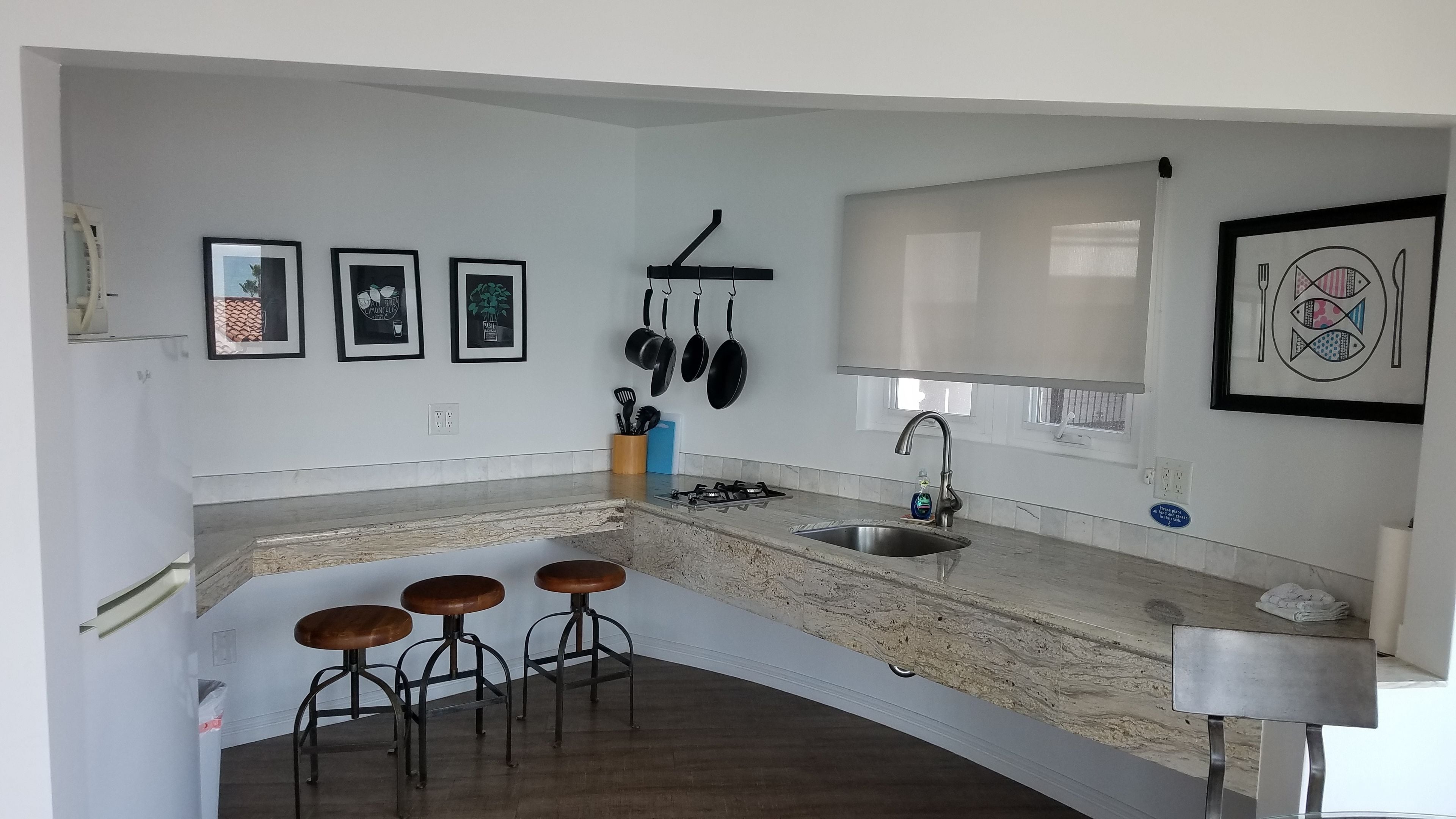 A modern kitchen with a granite countertop, a gas stove, a sink, and three bar stools.
