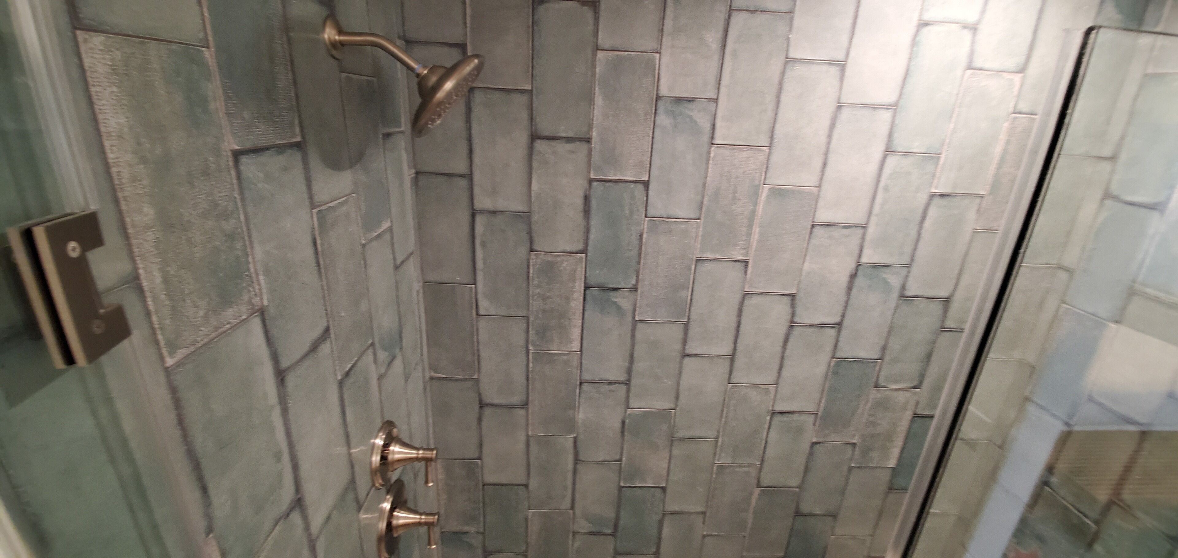 A shower area with a tiled wall and a metal showerhead.