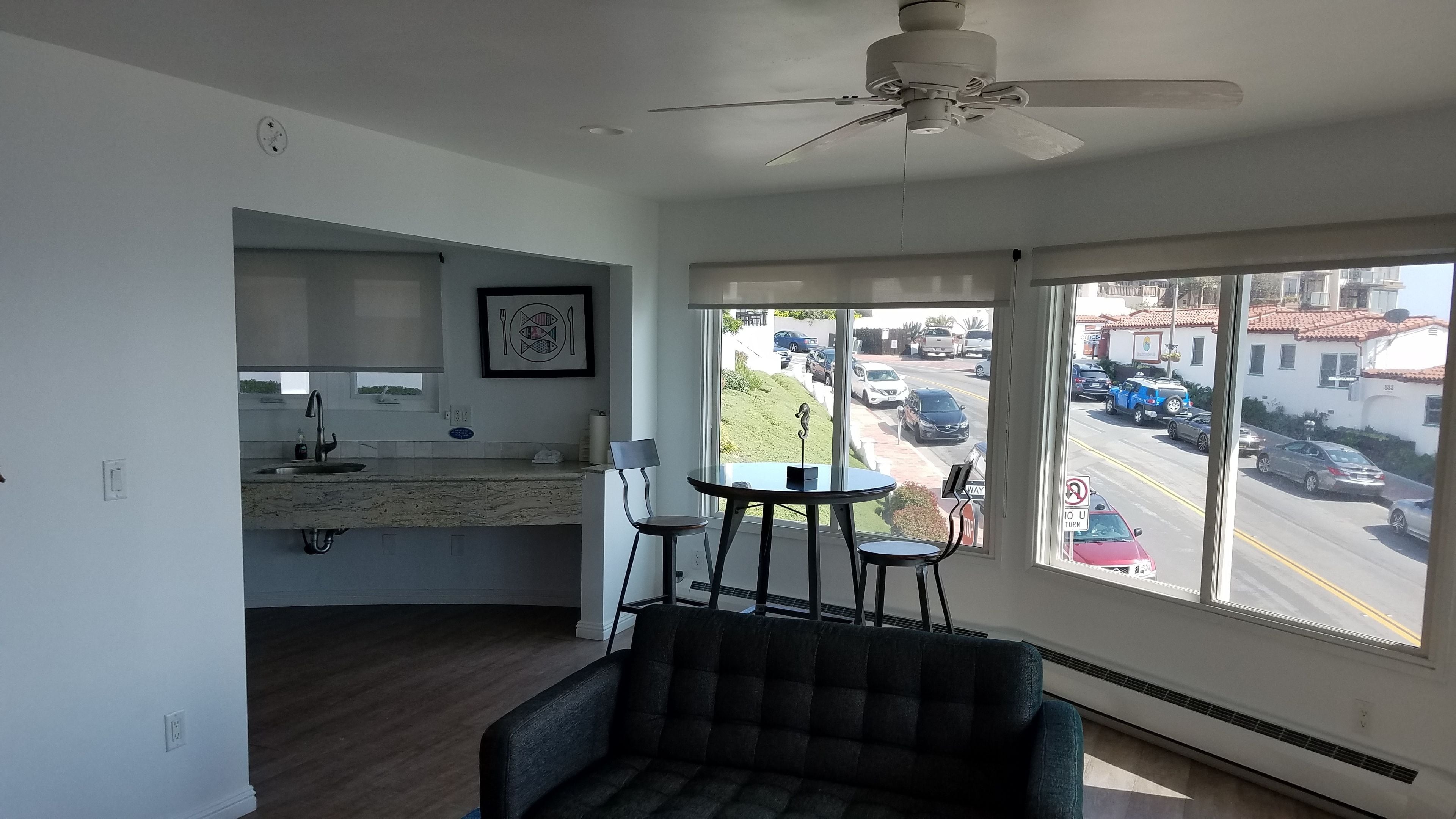 A modern kitchen with a built-in oven, a dining area with a table and chairs, and a large window offering a view of the street.