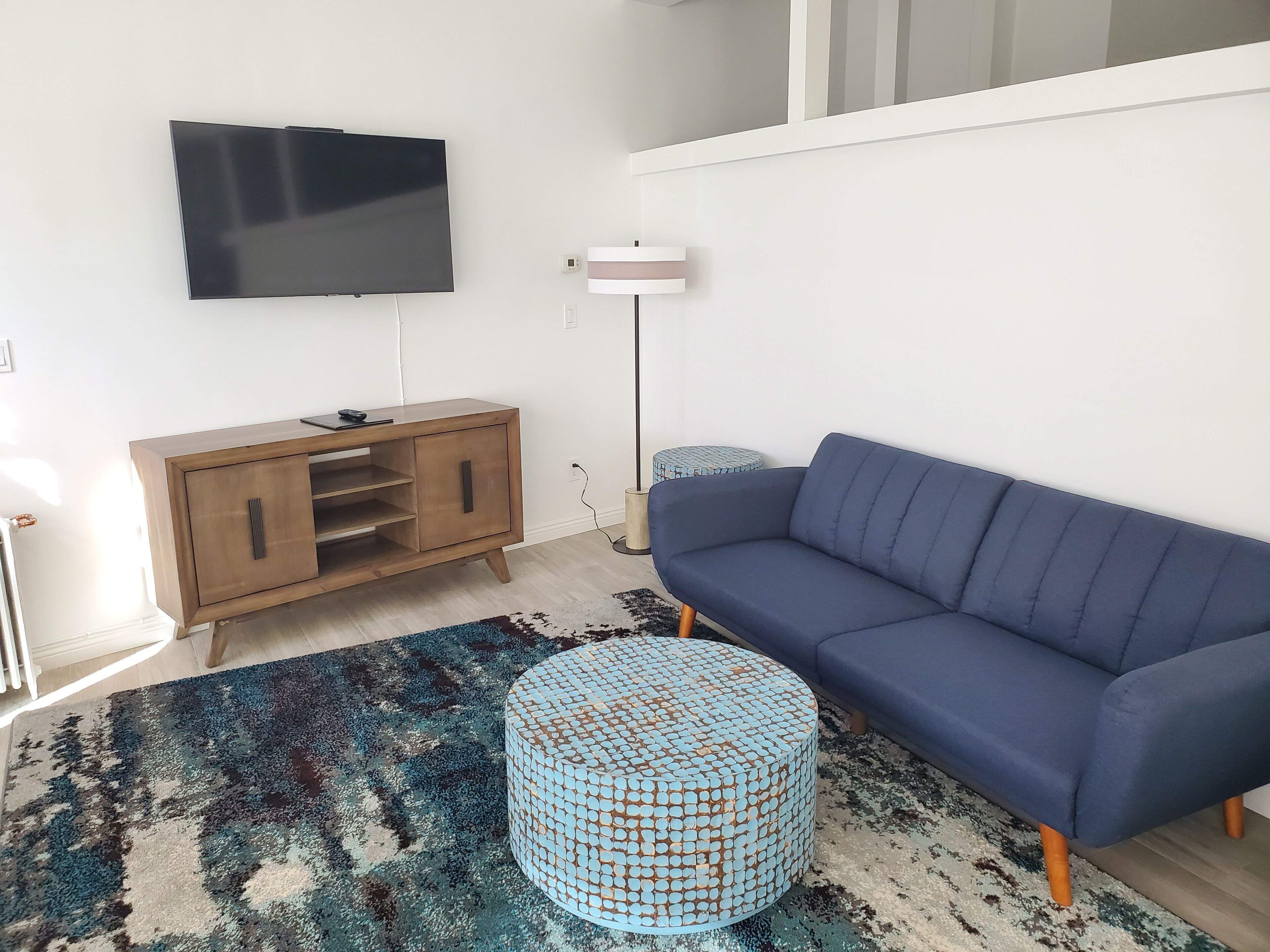 Una sala de estar moderna con un sofá azul oscuro, un mueble de entretenimiento de madera y una alfombra estampada.