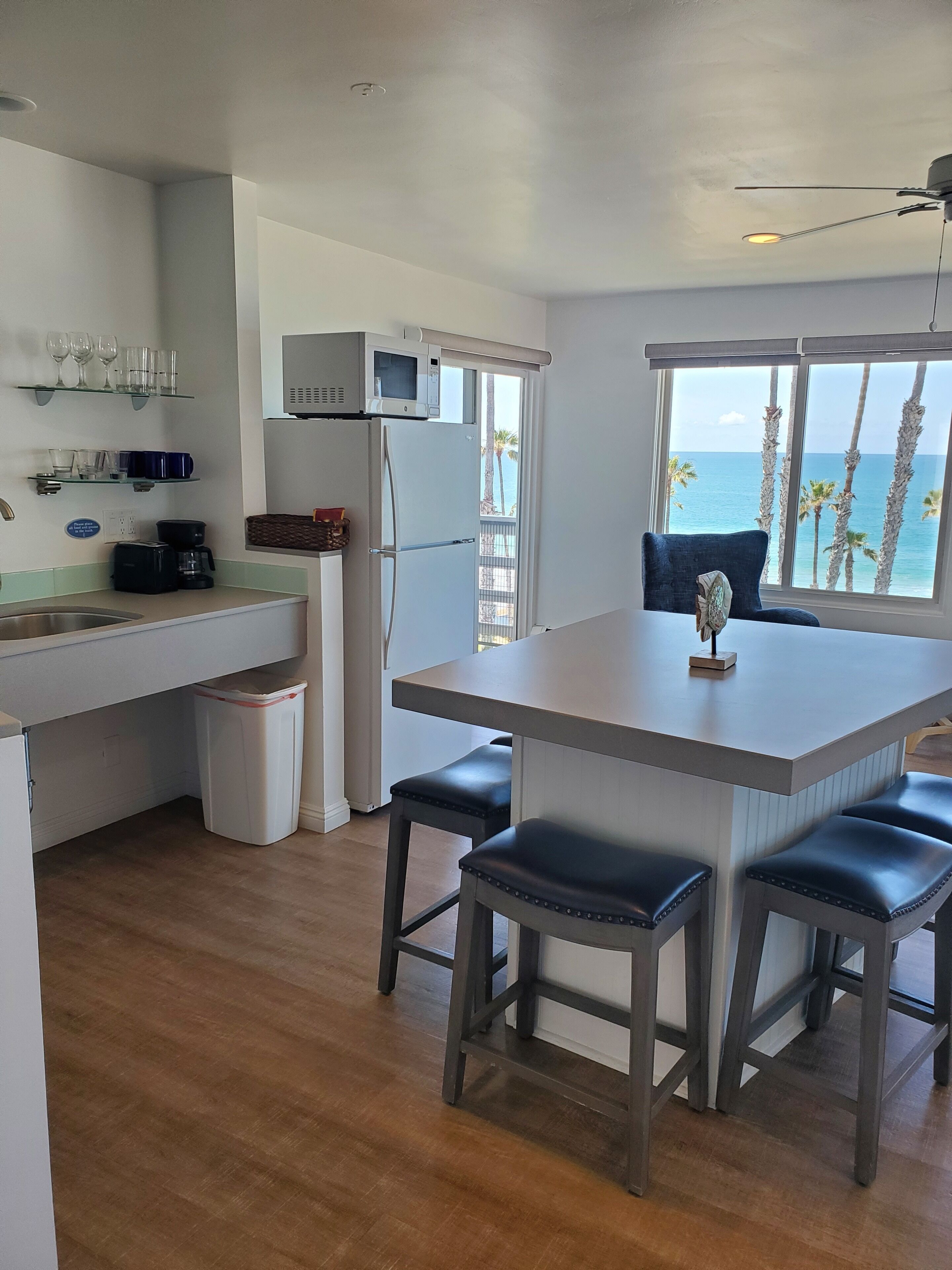 A modern kitchen with a central island, bar stools, a coffee maker, and a view of the ocean through large windows.