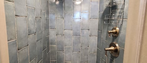Ducha con cabezal de ducha tipo lluvia y cabezal de ducha manual, un toallero de metal y un desagüe.