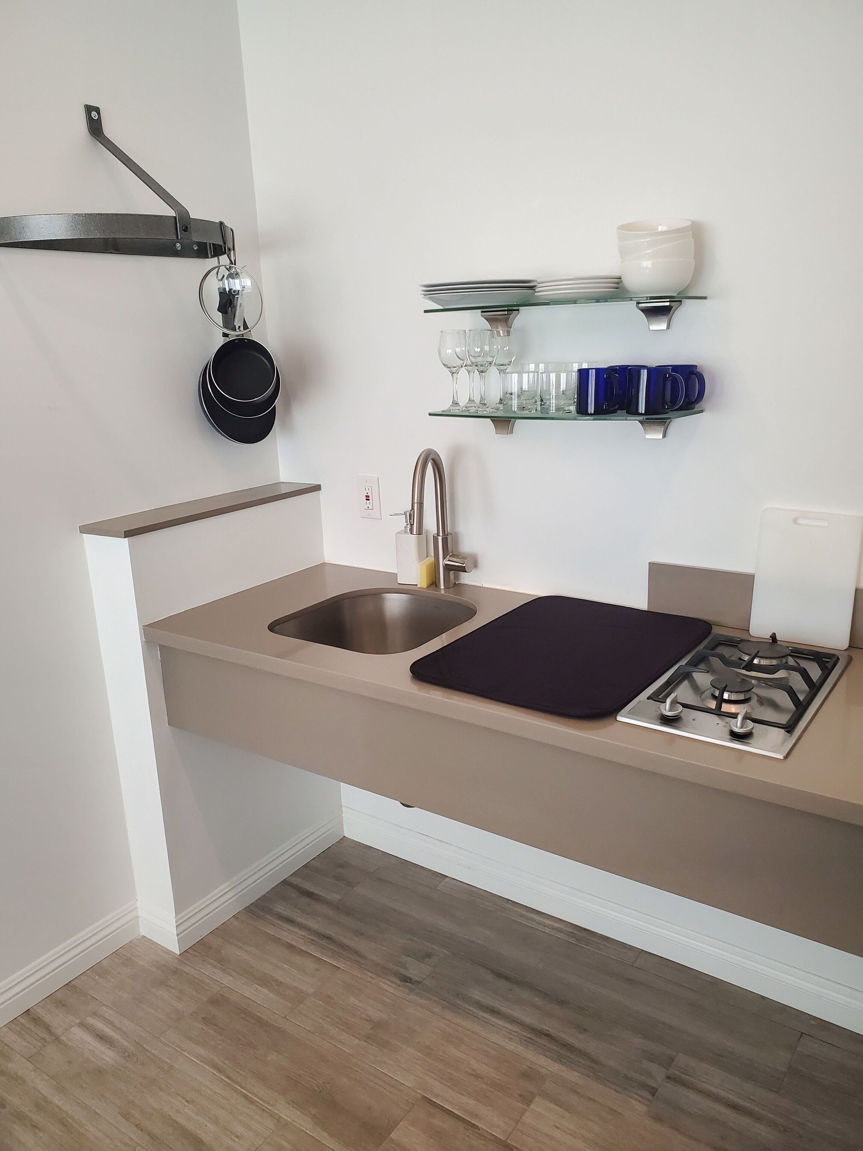 A kitchen with a double sink, stainless steel faucet, and a gas stove. There are shelves above the sink holding glassware and a pot rack with cookware.