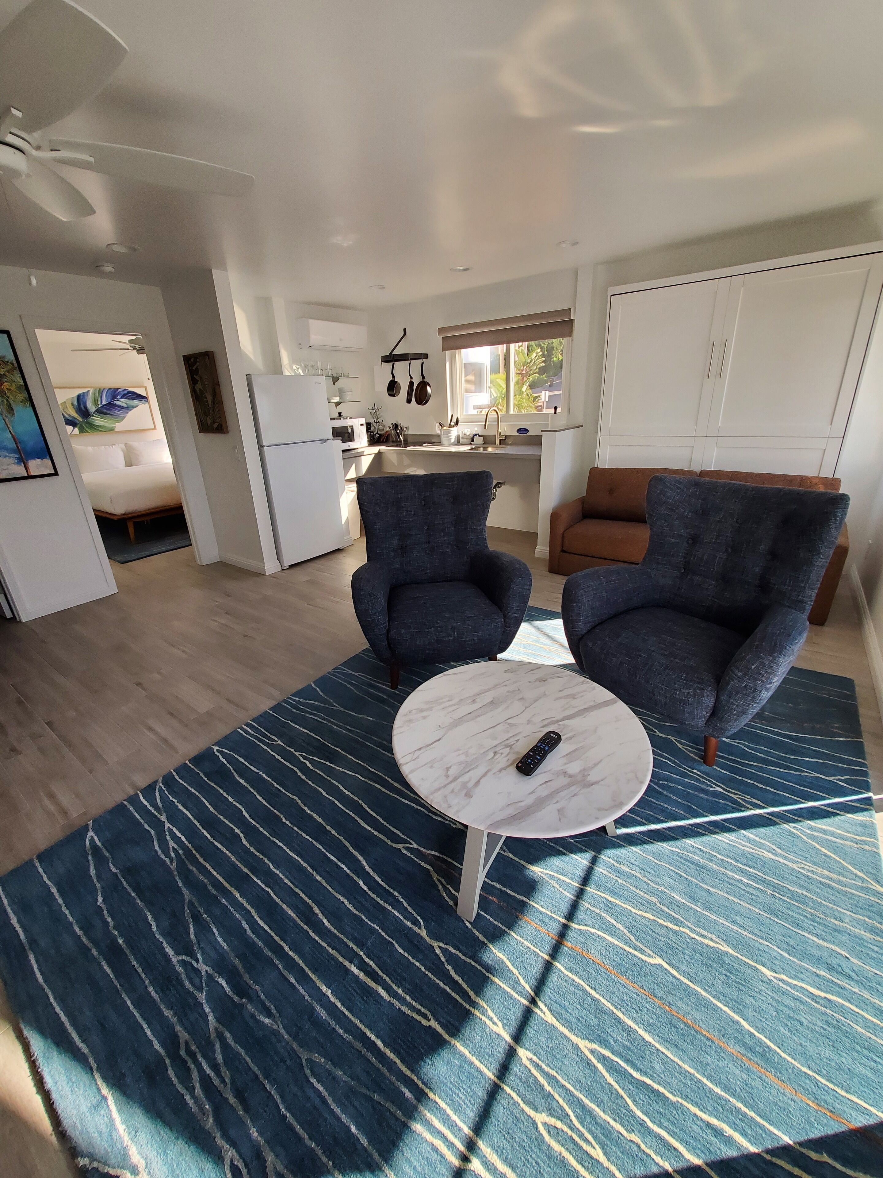 A modern living room with two dark armchairs, a round marble coffee table, and a kitchen in the background.