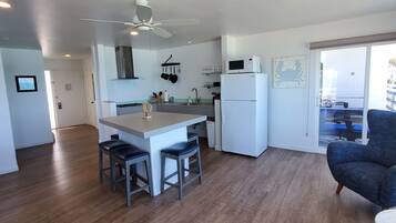 Una cocina moderna con una isla central, taburetes de bar, ventilador de techo y un comedor con una silla.