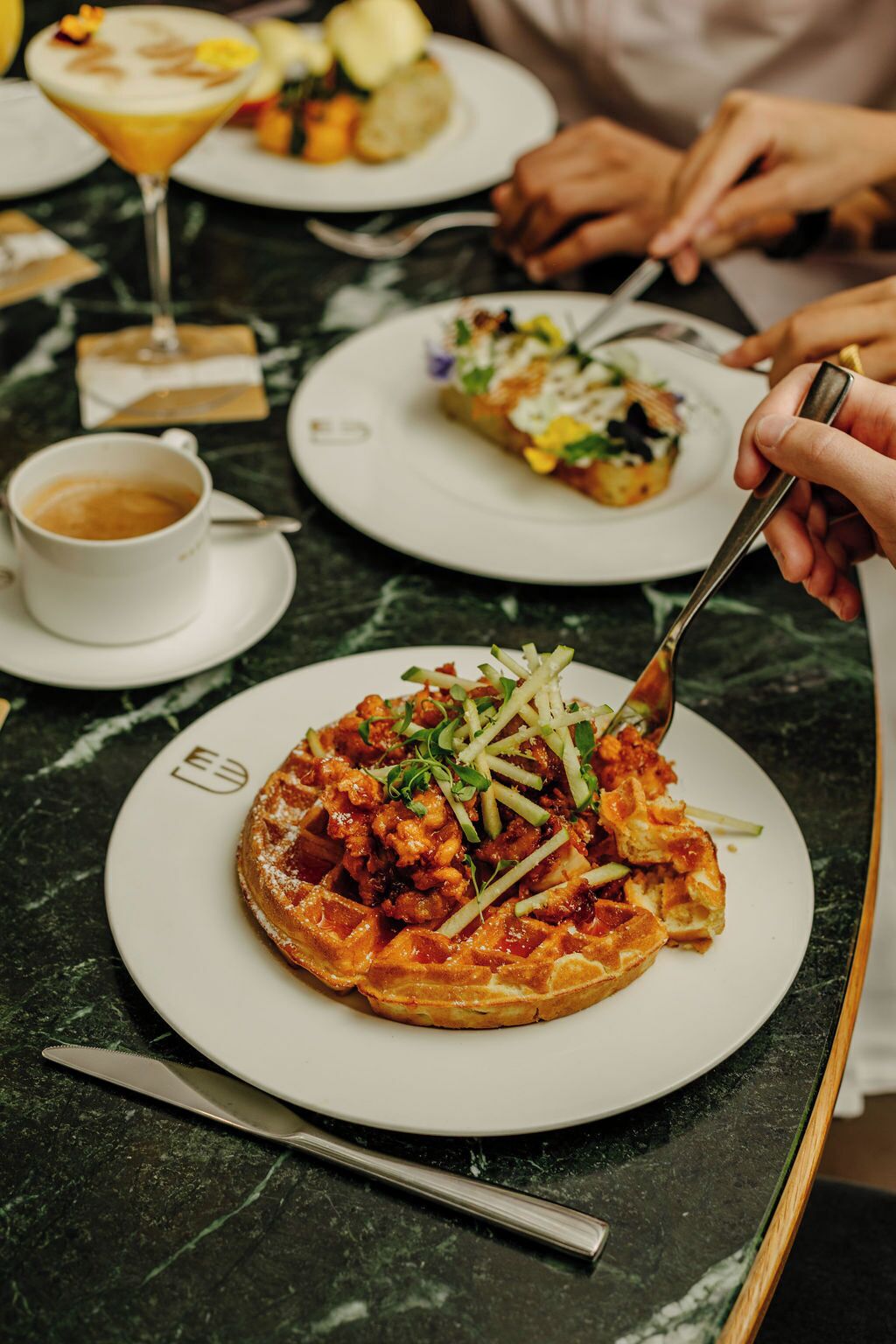Une table à manger avec des assiettes de nourriture, une tasse de café et un verre à martini.