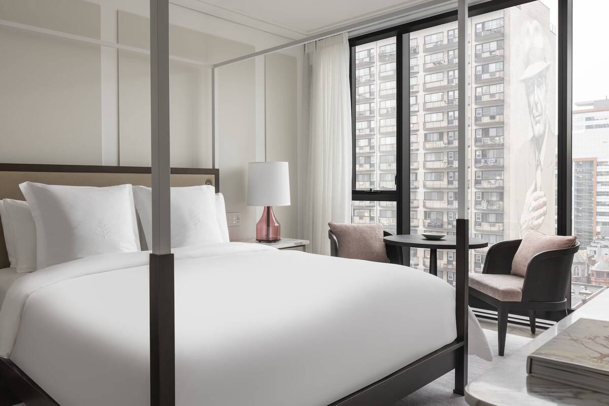 Una habitación de hotel moderna con cama con dosel, un escritorio con silla y un ventanal con vistas a la ciudad.