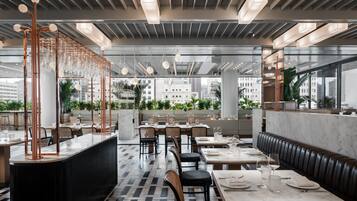 Un restaurante moderno con barra central, mesas de comedor y un área de estar con vistas a la ciudad.