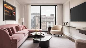 Ein modernes Hotelzimmer mit einem rosafarbenen Sofa, einem runden Couchtisch, einem beigefarbenen Sessel und einem großen Fenster mit Blick auf die Stadt.