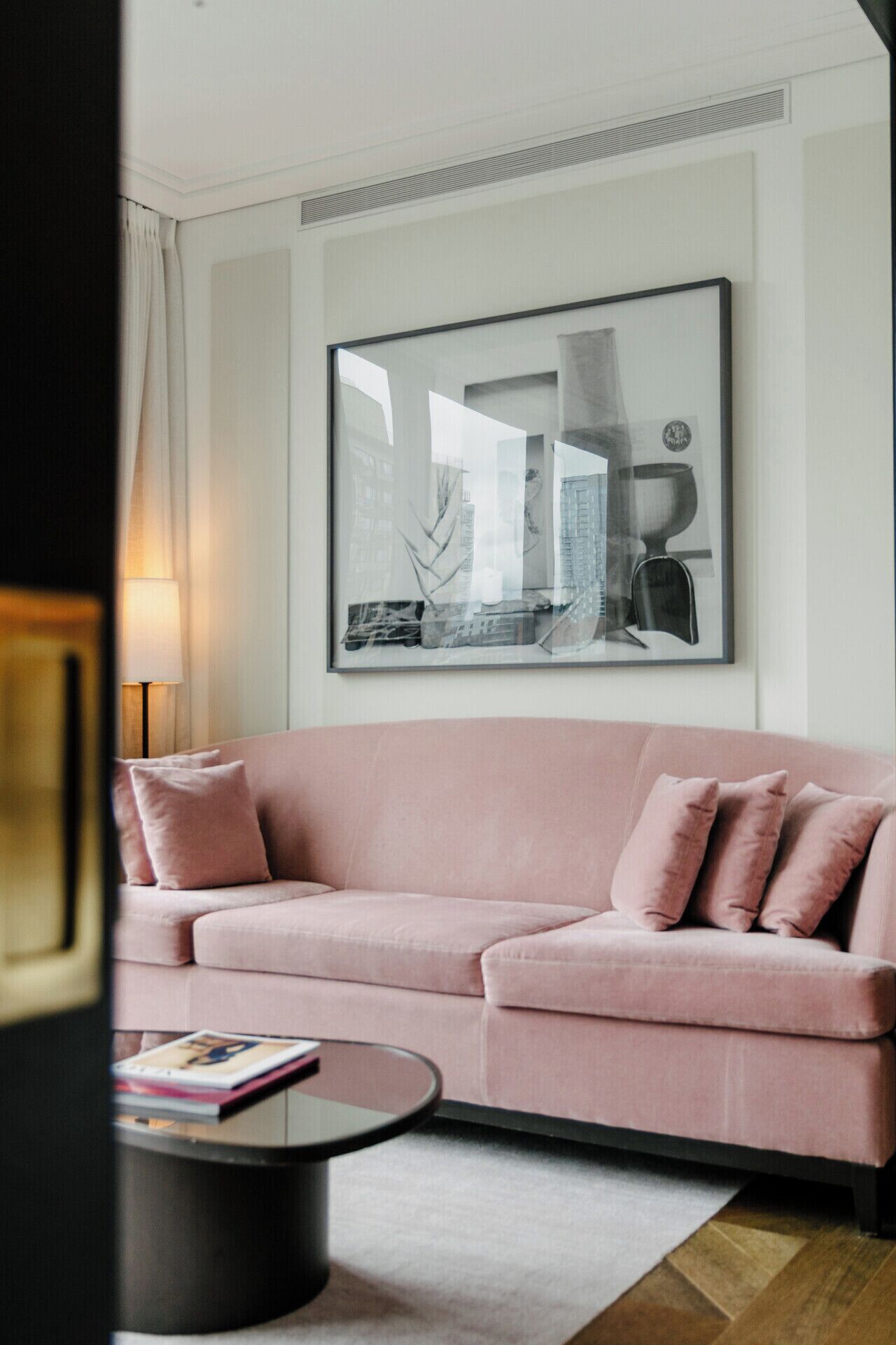 A modern living room with a pink sofa, a round coffee table, and a large framed artwork on the wall.