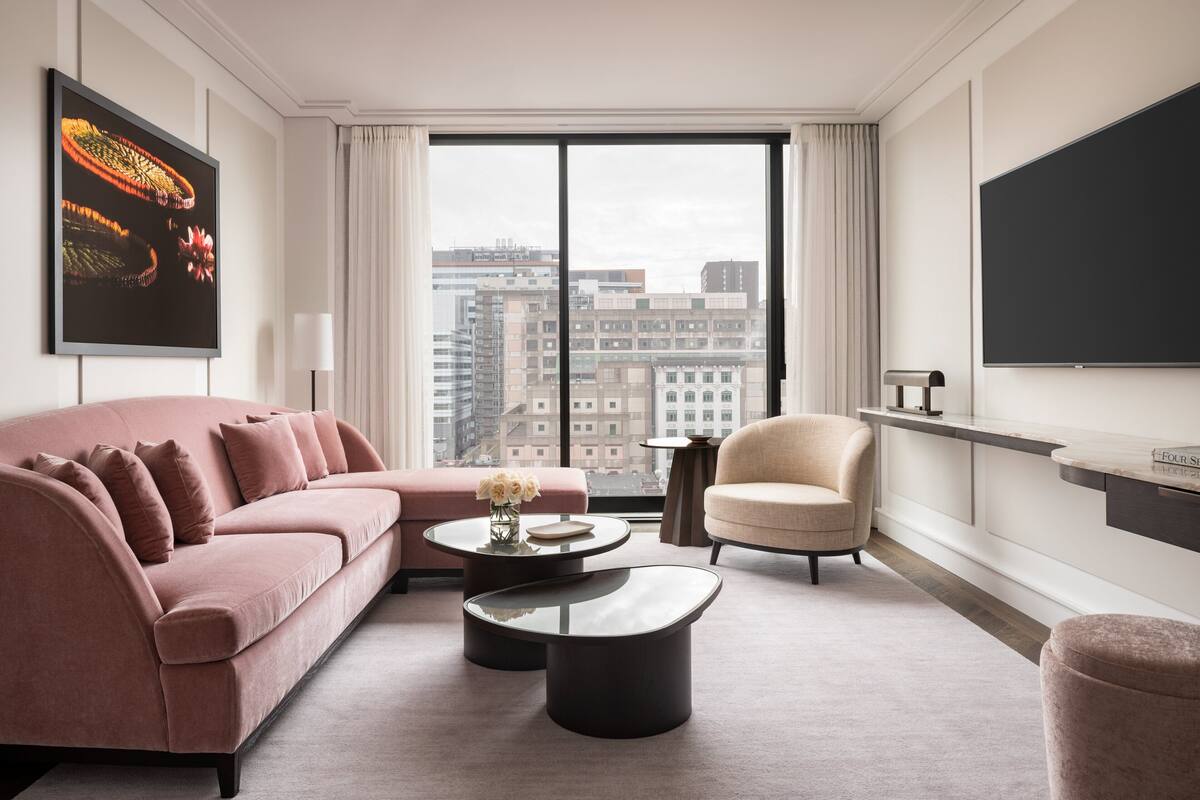 Una sala de estar moderna con un sofá rosa, una mesa de centro redonda y un sillón color beige. Un ventanal ofrece vistas a la ciudad.