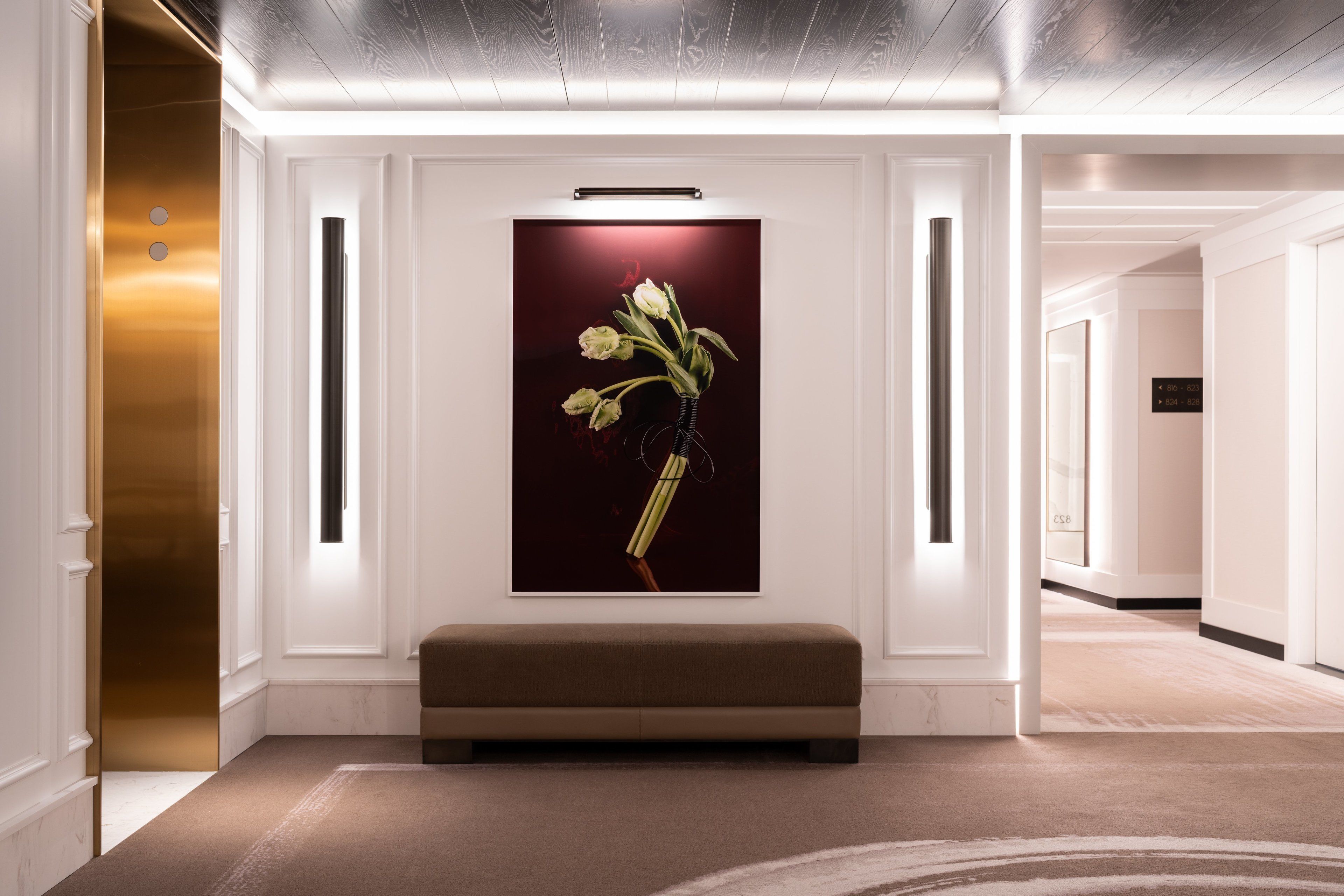 Un vestíbulo moderno con un banco, una obra de arte enmarcada de flores y un mostrador de recepción.
