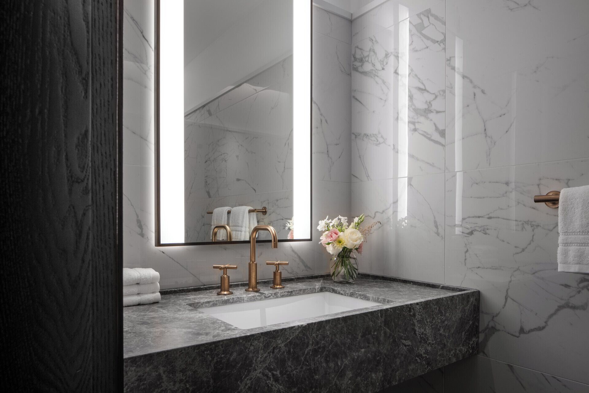 A bathroom with a marble sink, gold faucets, and a large mirror.