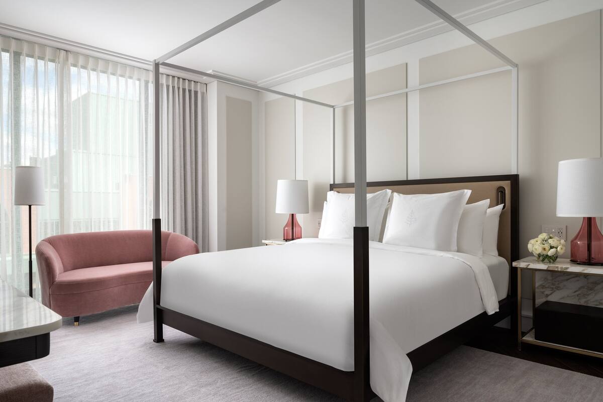 Una habitación de hotel moderna con una cama grande, un sillón de descanso y una mesita de noche de mármol.