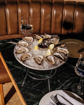 A dining table with a plate of oysters on ice, a glass of red wine, and a glass of white wine. - Four Seasons Hotel Montreal (Montreal)