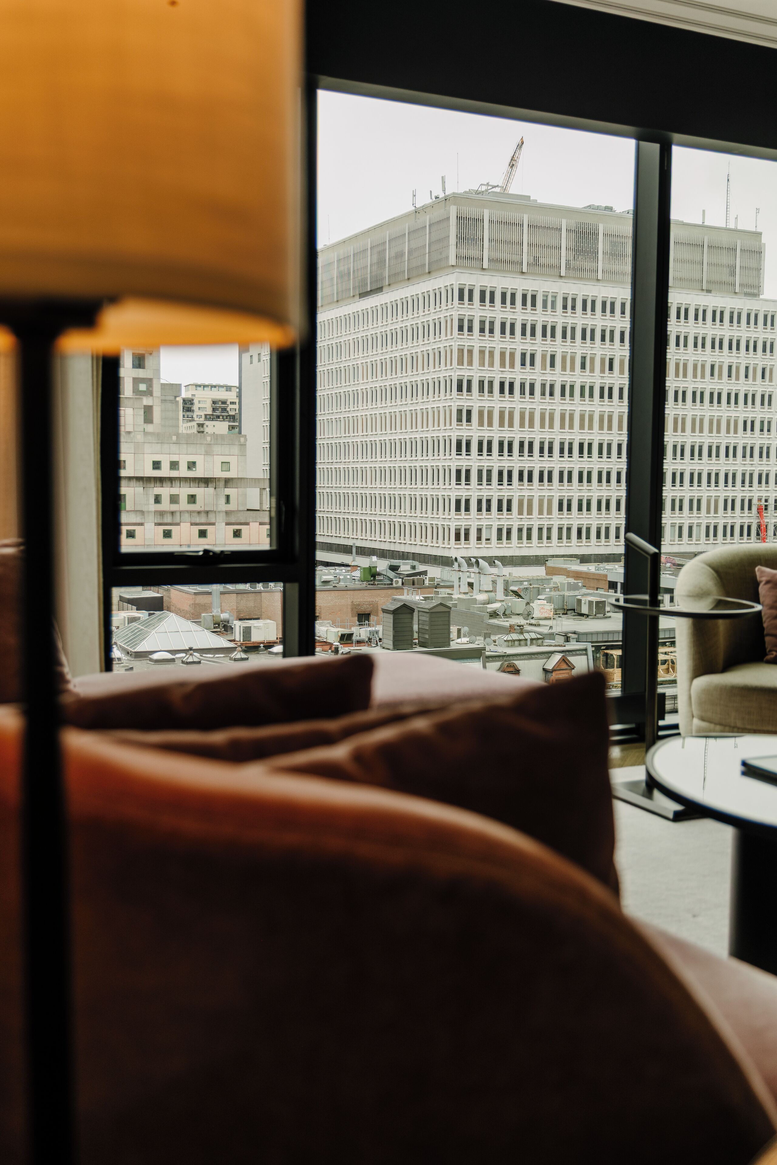 A modern hotel room with a large window offering a view of a cityscape, including a distinctive building with a crane.