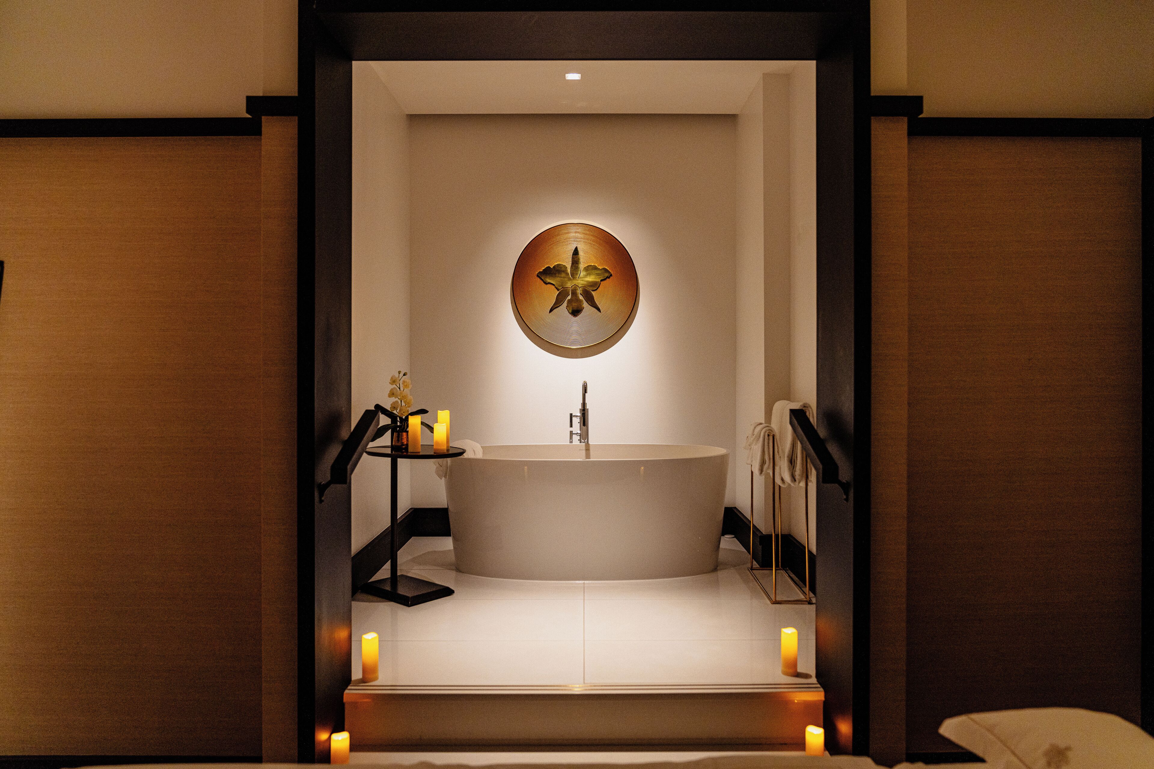 Une salle de bain moderne avec une baignoire sur pieds, un miroir rond et des bougies posées sur le sol.