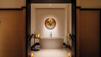 A modern bathroom with a freestanding bathtub, a round mirror, and candles on the floor.