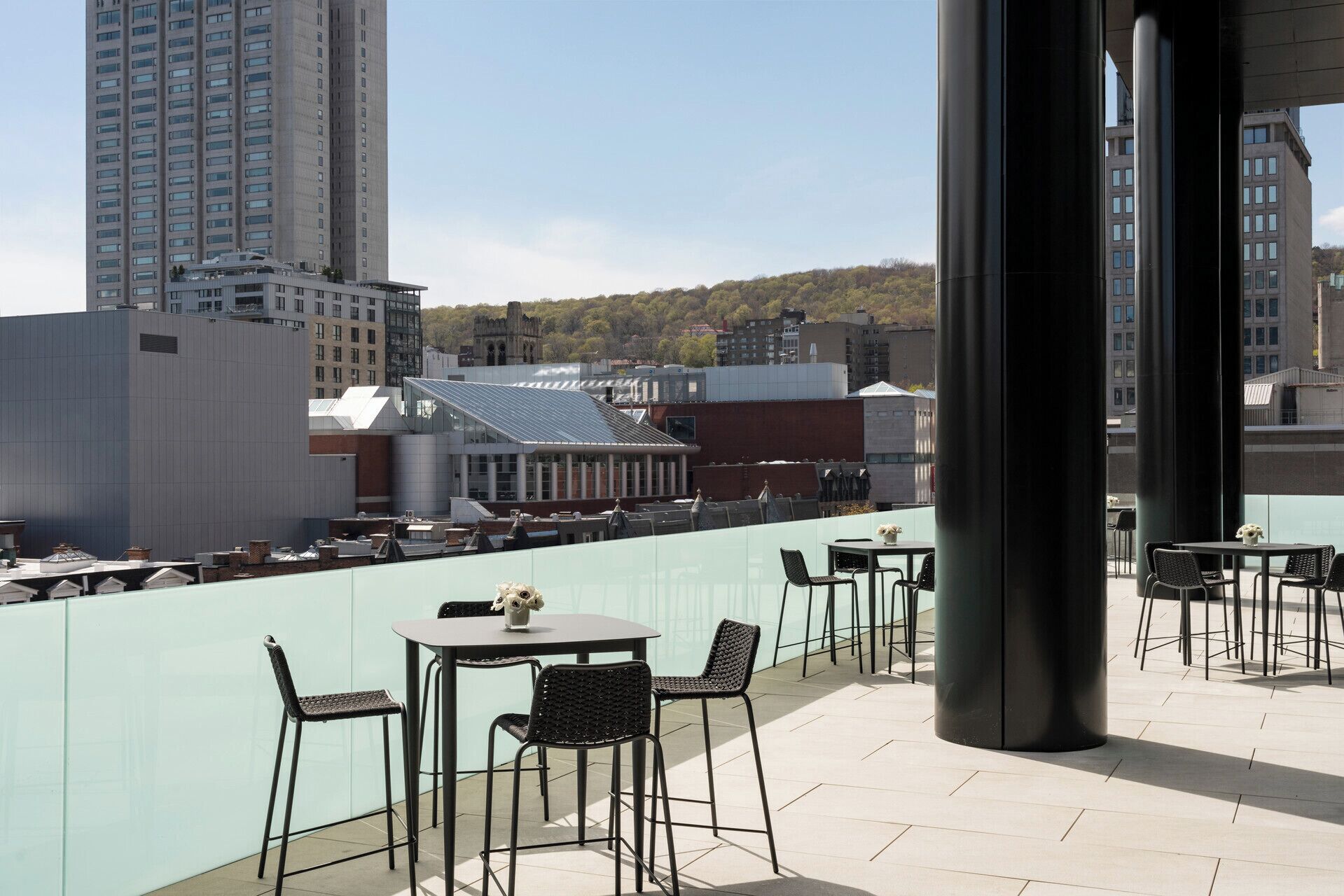 Terraza en la azotea con mesas y sillas, con vistas a un paisaje urbano que incluye edificios y una colina.