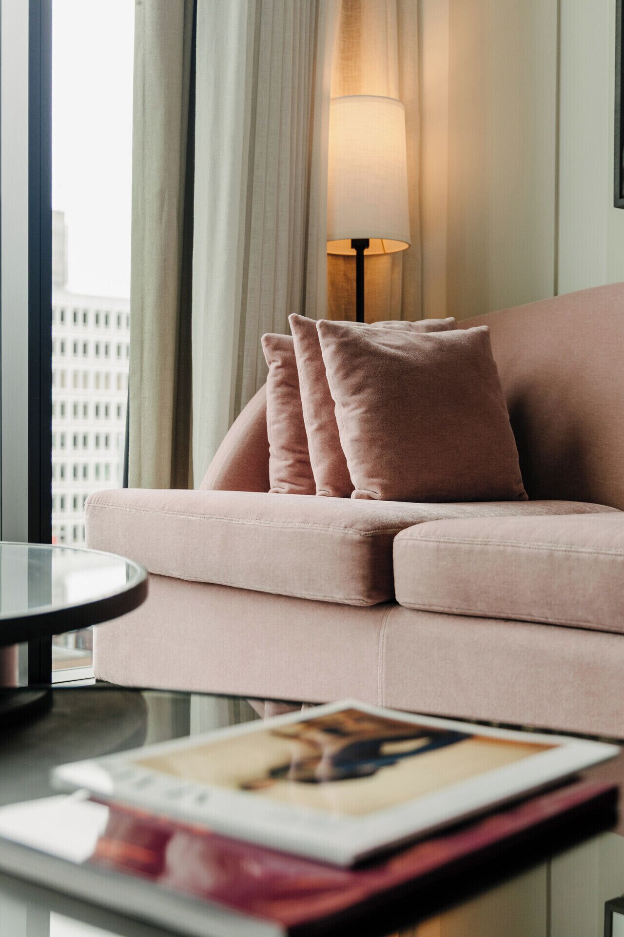 Un salon moderne avec un canapé rose, une table basse ronde en verre et un lampadaire.