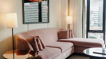 Una sala de estar moderna con un sofá seccional rosa, dos mesas auxiliares, una mesa de centro de vidrio y un ventanal con vista a la ciudad.
