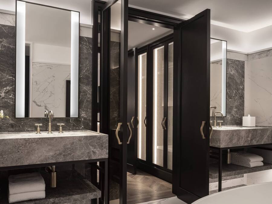 Un baño moderno con dos lavamanos de mármol, un espejo grande y una ducha a ras de suelo.