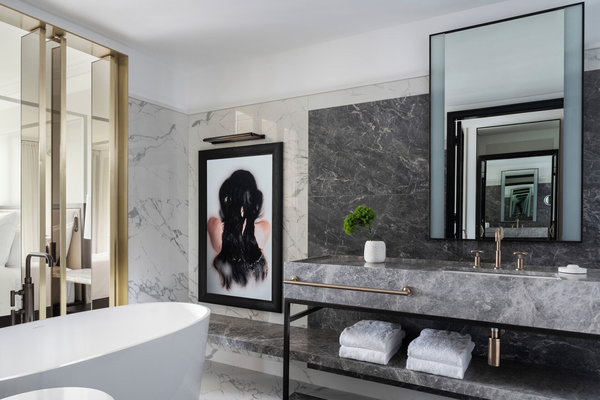 A modern bathroom with a marble vanity, a large mirror, a framed artwork, and a bathtub.