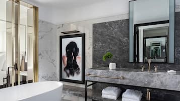 A modern bathroom with a marble vanity, a large mirror, a framed artwork, and a bathtub.