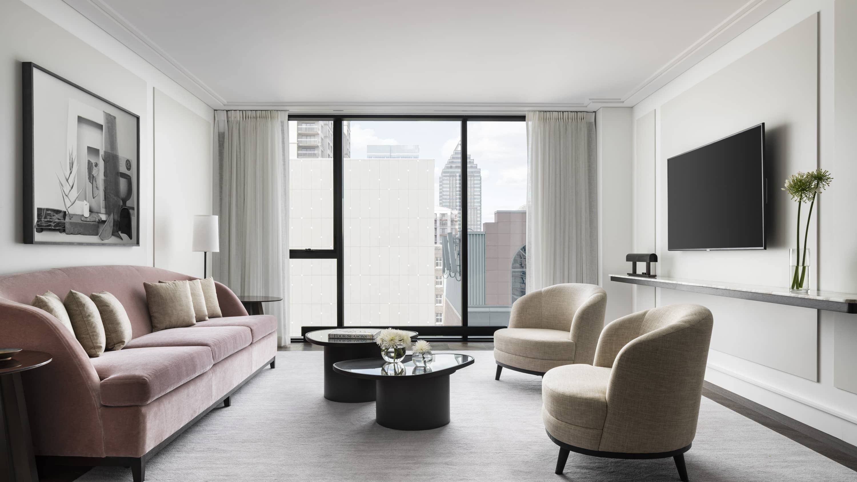 Una sala de estar moderna con un sofá rosa, sillones beige, una mesa de centro y un televisor montado en la pared.