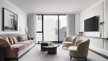 Una sala de estar moderna con un sofá rosa, sillones beige, una mesa de centro y un televisor montado en la pared.