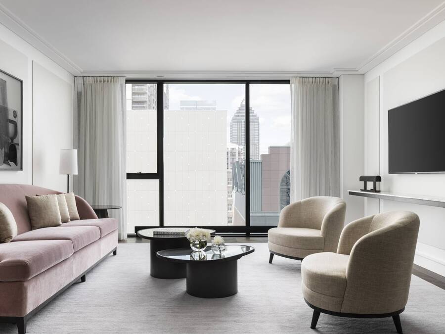 Una sala de estar moderna con un sofá rosa, sillones beige, una mesa de centro y un televisor montado en la pared.