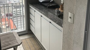 A small kitchen with a granite countertop, white cabinets, and a window overlooking a cityscape. - Ap Brás Templo Salomão 25 Março (São Paulo)