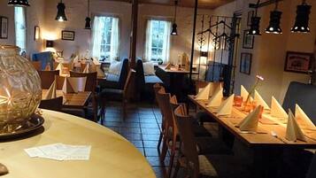 Un restaurante acogedor con mesas y sillas de madera, y lámparas colgantes.