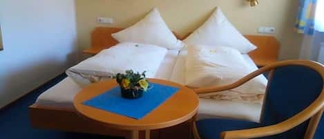 Una habitación de hotel con una cama, una mesita con un florero y una silla.
