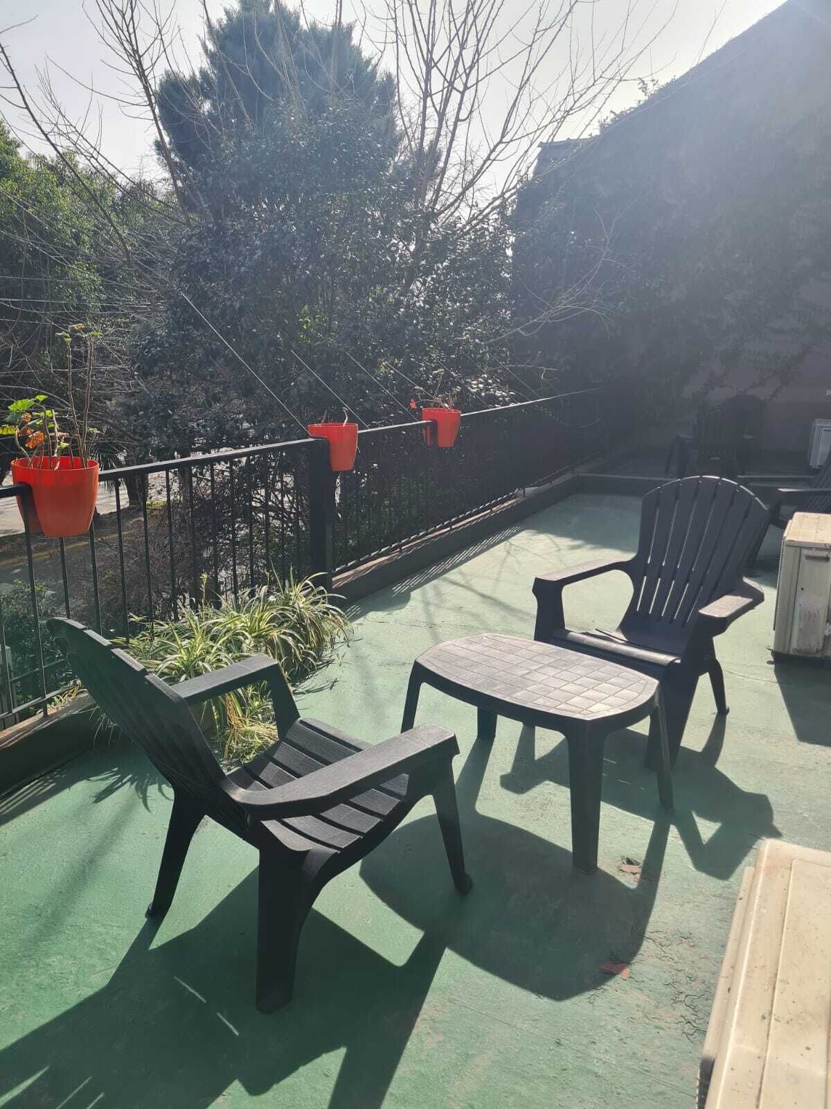 A patio area with two chairs and a table, surrounded by a green railing with potted plants.