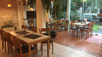 A restaurant with wooden tables and chairs, potted plants, and a brick wall.
