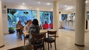 Ein Restaurant mit großen Fenstern, einer Rezeption und mehreren Tischen mit Stühlen.