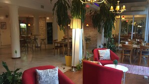 Eine großzügige Lobby mit roten Sesseln, einer Ziegelwand, hängenden Pflanzen und einer modernen Kristallleuchtre.'
