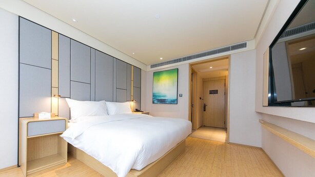 Une chambre d’hôtel moderne avec un grand lit, des tables de chevet, un tableau et une vue sur le couloir.